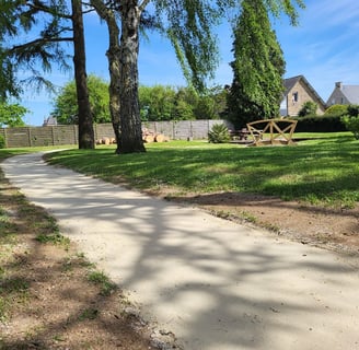 Allée en sable stabilisé sinuant à travers un jardin paysager arboré avec mobilier extérieur