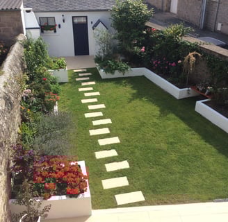 Jardin paysager avec gazon, massifs fleuris et pas japonais menant à une entrée de maison