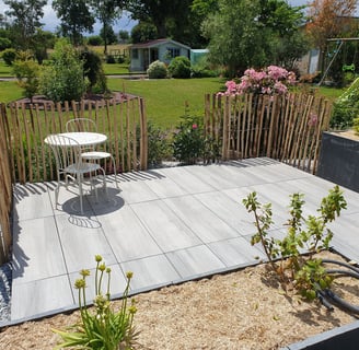 Petite terrasse carrelée avec mobilier de jardin, bordée d'une palissade en bois naturel