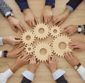 Hands of diverse professionals collaborating to connect wooden gears, symbolizing teamwork