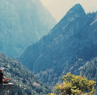 Woman meditating to relieve her mental health atop of a cliff within a mountain of forest
