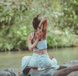 a woman sitting on a rock in a river practicing yoga as she knows her mental health will be boosted