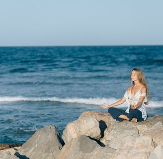 woman meditating on top of a rock near the ocean to relax her mind and be mindful