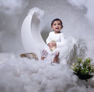 a baby sitting on a cloud with a flower in the foreground
