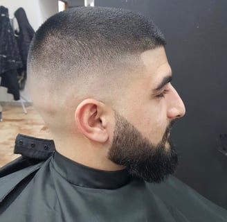 Taglio sfumato alto con barba rifinita su uomo con capelli corti e scuri, eseguito in salone da barb