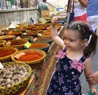 a little girl is standing in front of a table with a variety of spices