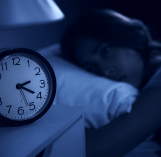 A woman lying in bed, unable to sleep, eyes fixed on her alarm clock
