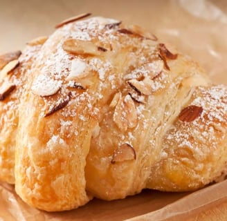 Golden almond croissant topped with sliced almonds and powdered sugar, resting on parchment paper