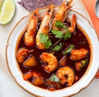 Caldo de Camaron in a bowl, featuring shrimp in a rich red broth, garnished with cilantro and served with lime wedges
