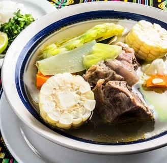 Traditional caldo de res served in a bowl with tender beef, fresh vegetables, corn, and sides of ric