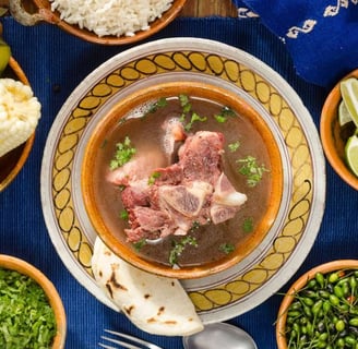 A hearty beef soup with corn, potatoes, squash, and rice, served with lime and tortillas