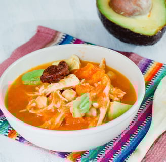 A chicken soup with chickpeas, avocado, and chipotle in a tomato-based broth