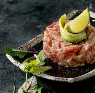 chicken tartare dish topped with avocado slices and lime, served with fresh mixed greens