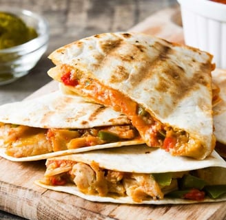 Chicken quesadilla slices garnished with fresh pico de gallo on a wooden tray, served with tomatoes and pickles