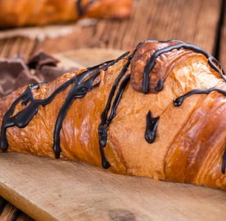 Freshly baked croissant drizzled with rich chocolate on a rustic wooden board