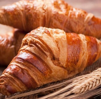 Freshly baked croissant along with wheat grains on a rustic wooden board