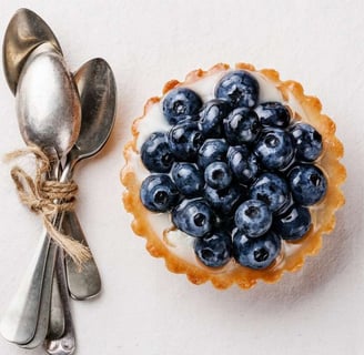 Elegant arrangement of vintage dessert spoons tied with twine, placed beside a blueberry tart with creamy filling