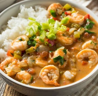 A bowl of Gumbo with shrimp, rice, and green onion garnish in a white bowl