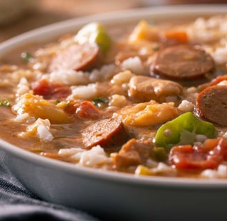 Gumbo highlighting shrimp, sausage, and colorful vegetables, served over white rice in a rich, savory sauce.