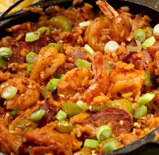 A rustic skillet filled with spicy Jambalaya, featuring seasoned rice, juicy shrimp, slices of sausage, and fresh green onion