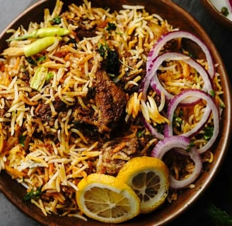 Mutton biryani garnished with onions, lemon, and chilies in a copper pot on a slate background