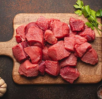 diced mutton pieces on a wooden cutting board, along with parsley, a garlic, peppercorns and Himalayan salt