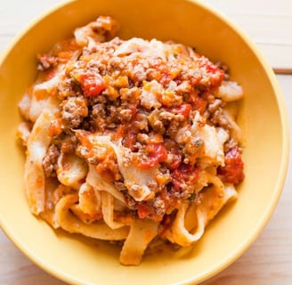 Pappardelle pasta topped with a rich and hearty Bolognese sauce served in a yellow bowl, perfect for authentic Italian dinner