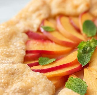 Freshly baked peach crostata featuring a flaky, golden crust, arranged with sliced peaches and topped with fresh mint leaves
