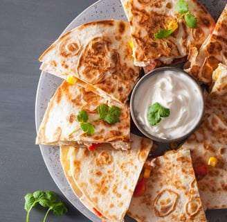 Classic quesadilla slices filled with cheese and vegetables, served on a plate with sour cream in the center, with cilantro