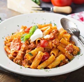 Rigatoni with creamy Bolognese sauce, cherry tomatoes, basil, and ricotta in a white bowl
