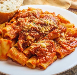 Rigatoni pasta smothered in a savory Bolognese sauce, garnished with Parmesan cheese, served with a slice of bread
