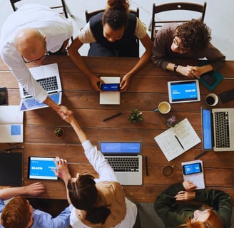 a group of people sitting around a table with laptops