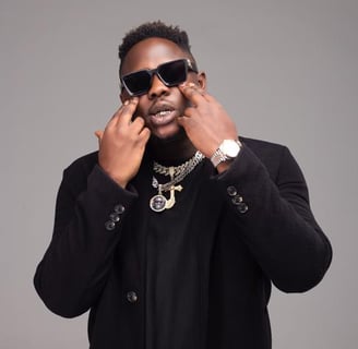 Medikal in sunglasses with chains on his neck.