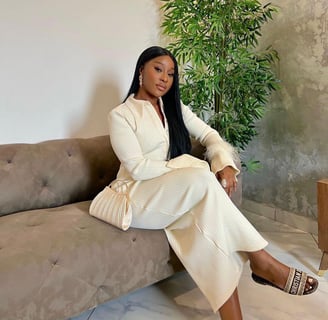 Efia Odo sitting on a couch dressed in a matching dress with a bag.