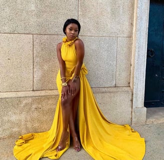 Efia Odo posed by a wall in a stunning yellow overall dress.