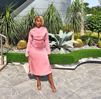 Efia Odo in a pink overall dress with a designer handbag.