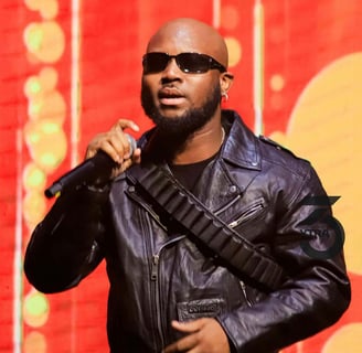 King Promise in a black jacket in sunglasses with a microphone.