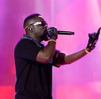 Sarkodie performing on stage in a black top and black shades.