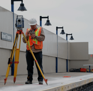 a man in a hard hat and safety vest using a tripod