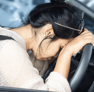 exhausted woman with head and hands resting on steering wheel
