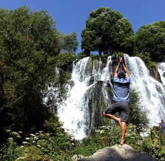 a man standing on a rock in front of a waterfall