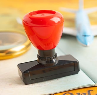 Red immigration stamp on passport with toy airplane and magnifying glass, symbolizing travel.