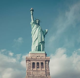 A close-up of the Statue of Liberty, standing tall with her torch raised against a clear blue sky.