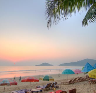 Beach with sunset and people walking along the beach with umbrellas to sit