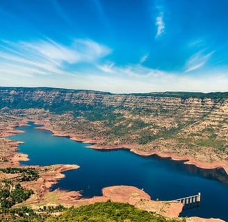 A water body surrounding with mountains and trees with blue sky