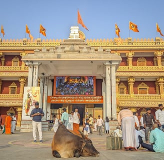 A temple complex with people standing outside the temple and flags at the top of the temple.