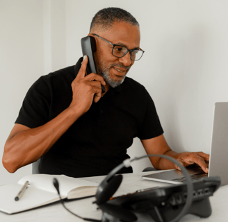 a man sitting at a desk with a laptop and a cell phone