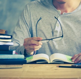 a man is sitting at a desk with a book and glasses