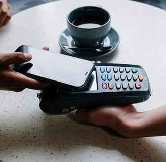 Person using a smartphone for contactless payment on a card reader with a coffee cup.