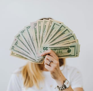 Person holding a fan of cash, displaying various U.S. dollar bills, covering their face.